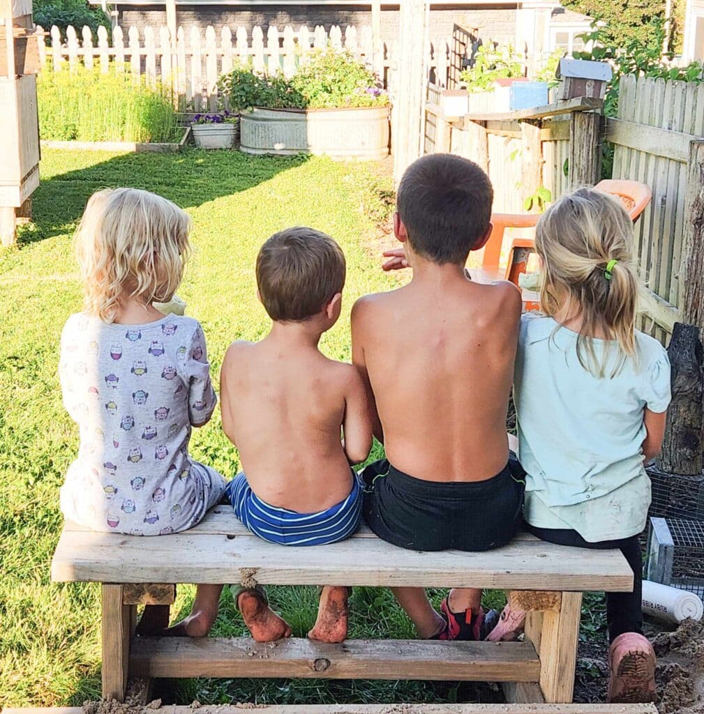 4 kids sitting on a bench with dirty feet outdoors
