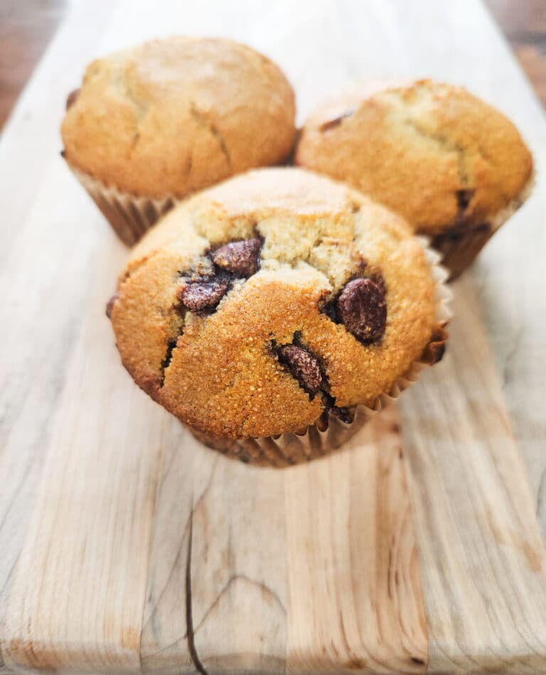 fresh milled flour sourdough chocolate chip muffins presented on a cutting board with 3 whole, puffy bakery style muffins