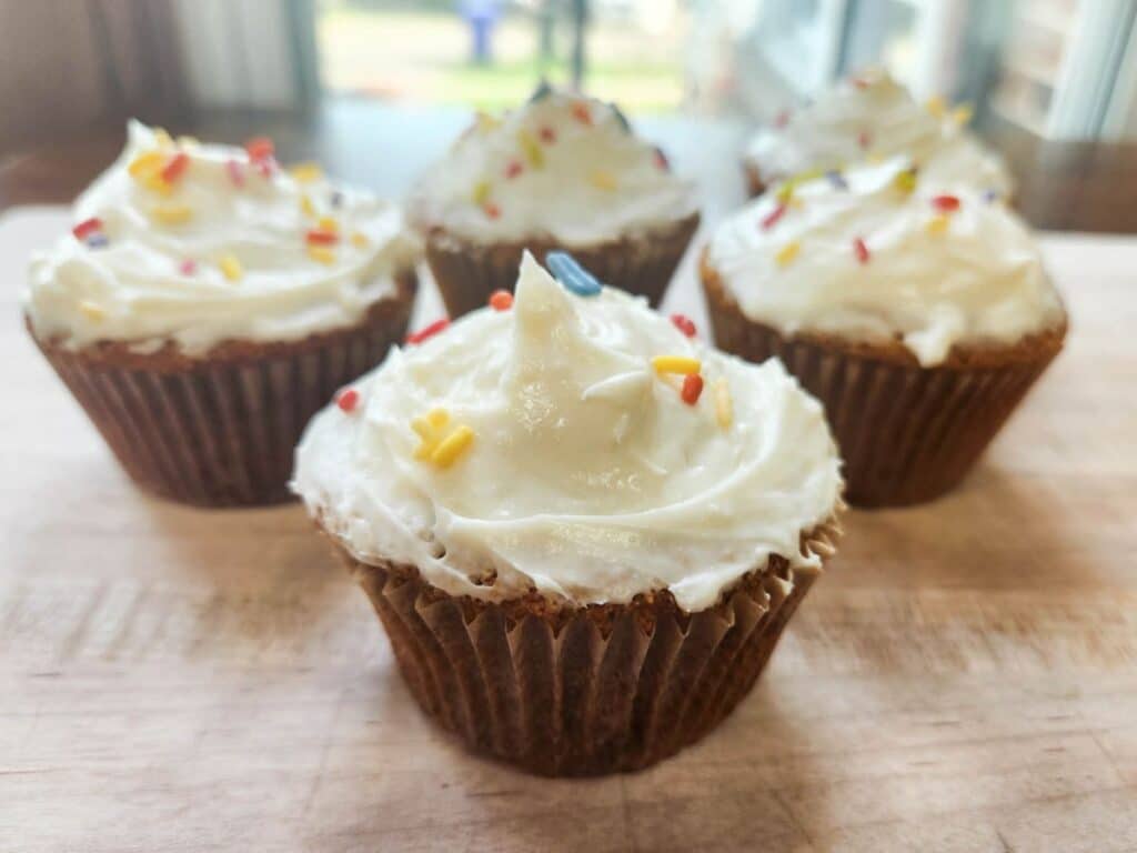 sourdough vanilla cupcakes with fresh milled flour, topped with whipped cream cheese frosting and dye free sprinkles, presented on a cutting board